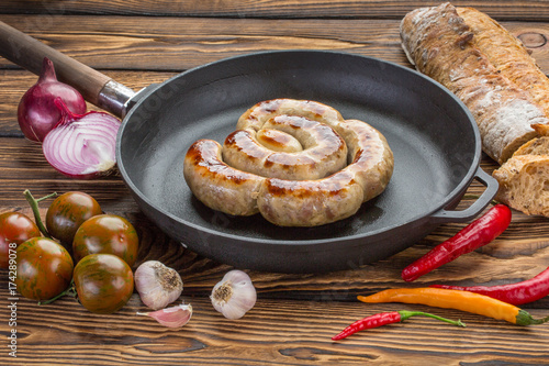 Frying pan with fried sausage, vagitables and bread over wooden background