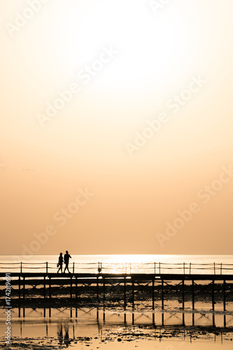 Silhouettes of the girl and the boy are walking along the pier at dawn