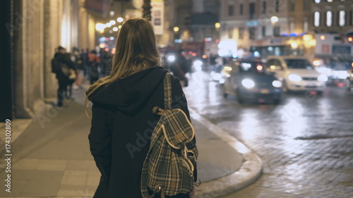 Fotografie Young traveling woman with backpack crossing the traffic road, tourist looking around and find the way in the evening
