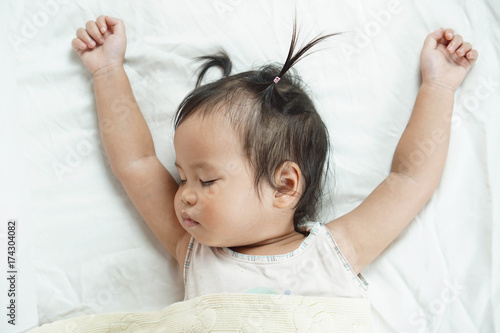 Cute toddler girl sleeping on white bed sheets cuddle in yellow blanket, bright room