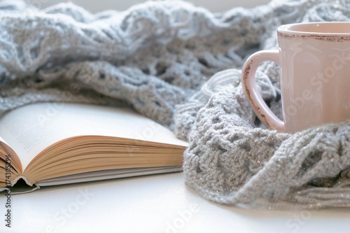 Cozy home still life: cup of hot coffee and opened book with warm plaid on windowsill against snow landscape outside. Winter holidays, Christmas time concept, free copy space photo