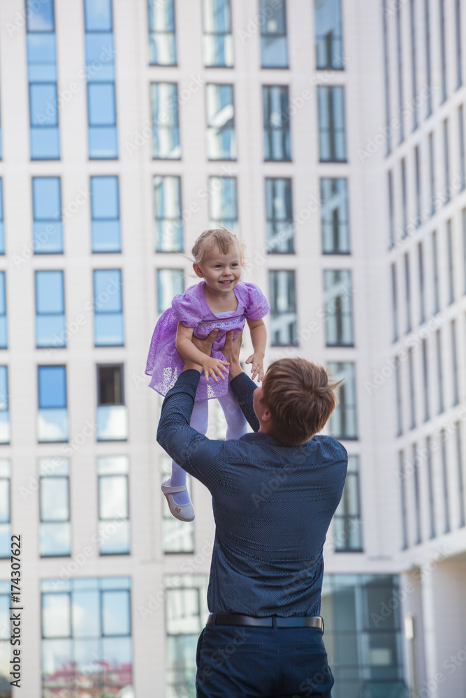 Father and daughter. Papa throws her daughter in the sky against the background of a glass building