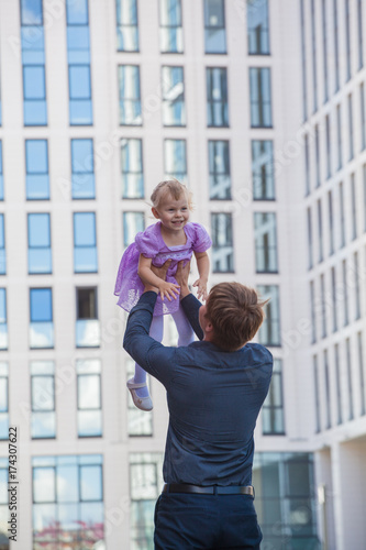 Father and daughter. Papa throws her daughter in the sky against the background of a glass building