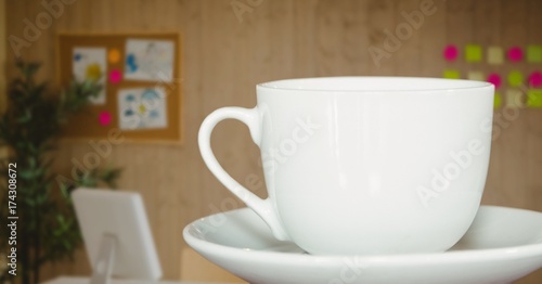 White coffee cup on saucer against blurry office with dark