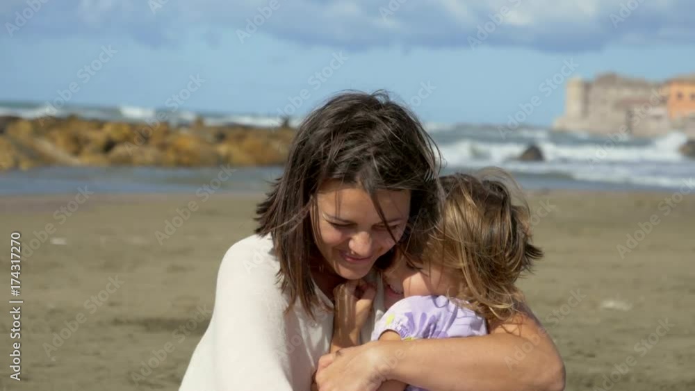 Woman and little daughter hugging tight on beach playing with dog Woman and little daughter hugging tight on beach playing with dog