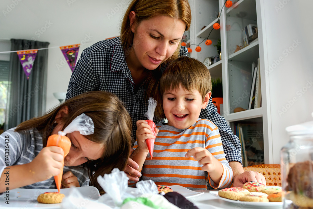 Naklejka premium Mother with kids decorating cookies for Halloween