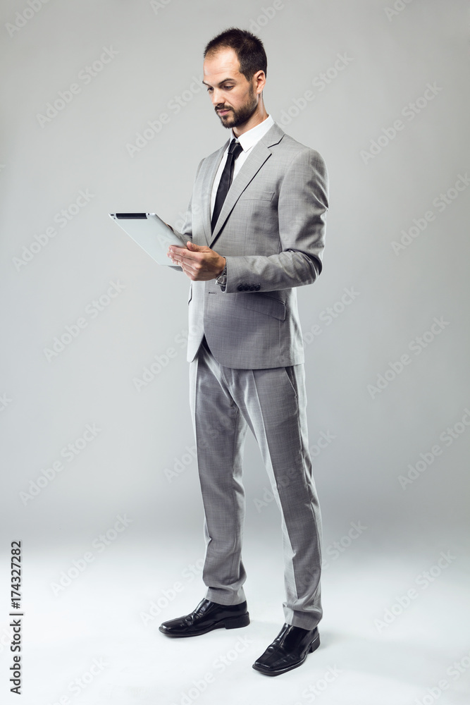 Business young man using his digital tablet over gray background. Business young man using his digital tablet over gray background.