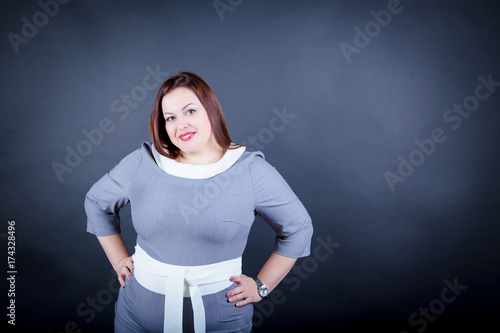 Fotografie Chubby  plus size woman  in a strict dress  is standing isolated on ablack backg