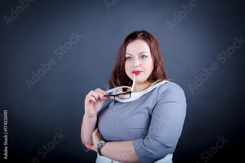 Obraz na plátně Chubby  plus size woman  in a strict dress  is standing isolated on ablack backg