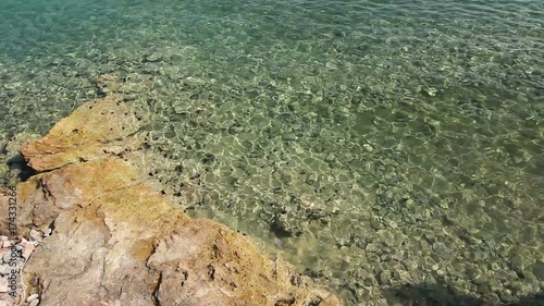 Rocky seafloor visible through crystal clear turquoise transparent rippling water. photo