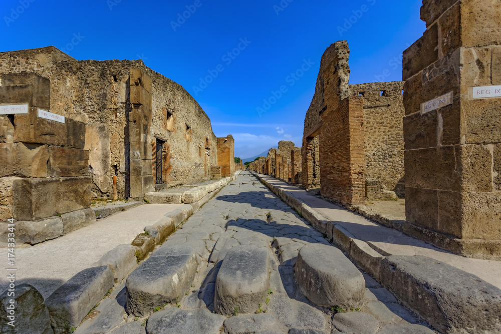 Italy. Ancient Pompeii (UNESCO World Heritage Site). Paving stones of Via Stabiana (Cardo Maximus street) with the blocks stone. There is Mount Vesuvius in the background