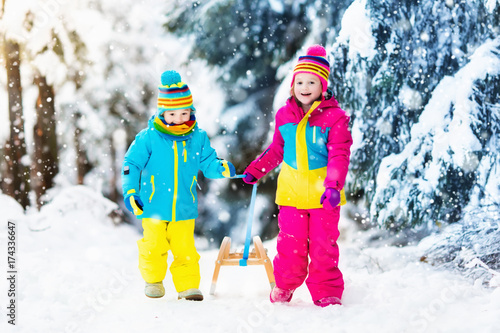 Children play in snow on sleigh in winter park
