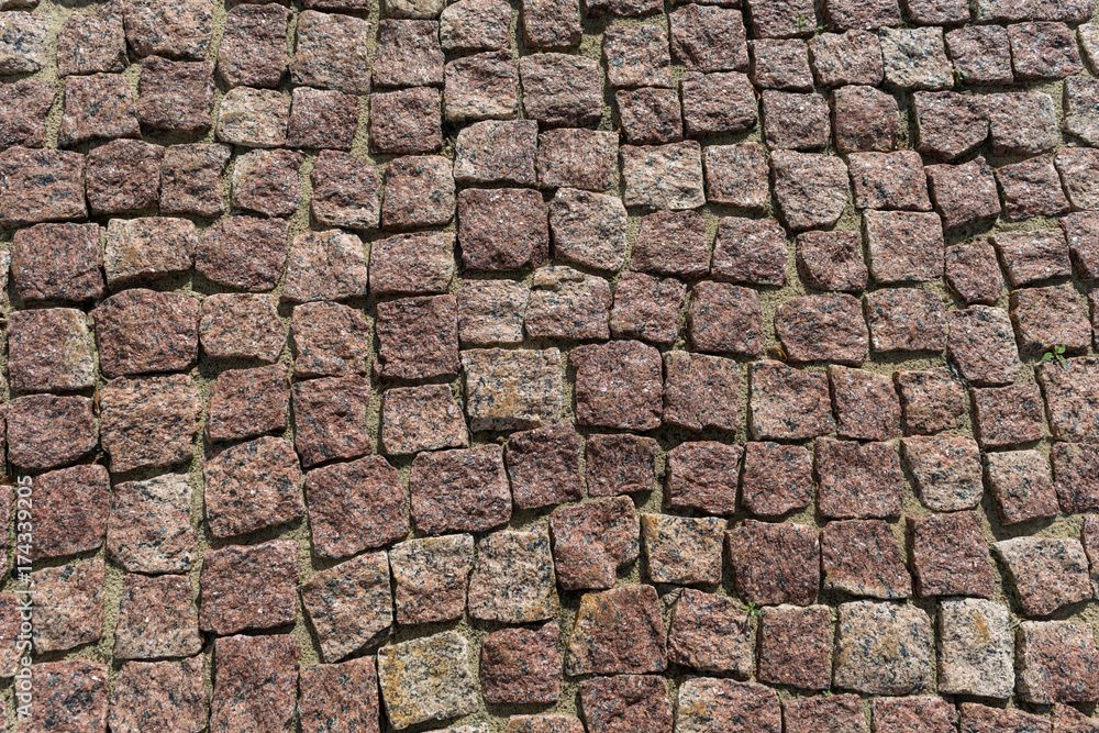 Square lined with cobblestone or stone pavement, walkway or road. The surface of rough stones and rough. Stones brown. Seams of sand. The cobbles have a mottled pattern and texture.
