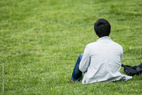 The young guy sits on the grass alone. The guy sits alone and stares into the distance. Place for text.