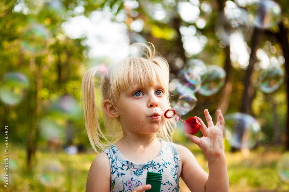 Cute little girl blows soap bubbles in park in summer Cute little girl blows soap bubbles in park in summer