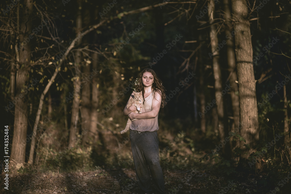 A young woman poses with her cat in the woods at sunset A young woman poses with her cat in the woods at sunset