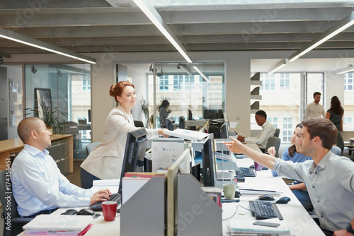 Female boss handing over document to employee in busy office