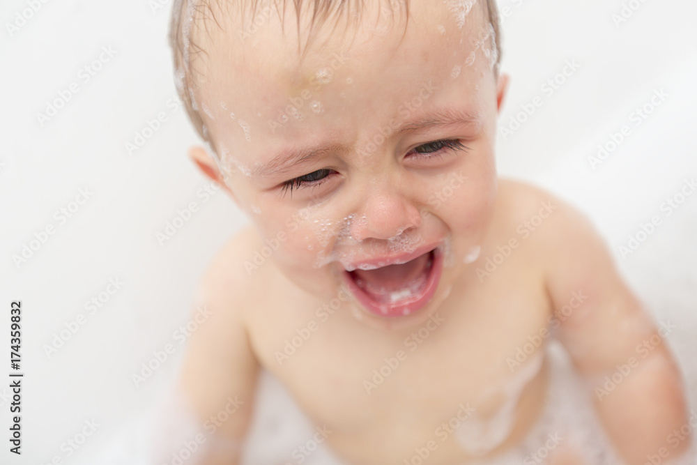 Crying baby by in a bathtub. Infant kid sreaming while taking a bath. Crying baby by in a bathtub. Infant kid sreaming while taking a bath.