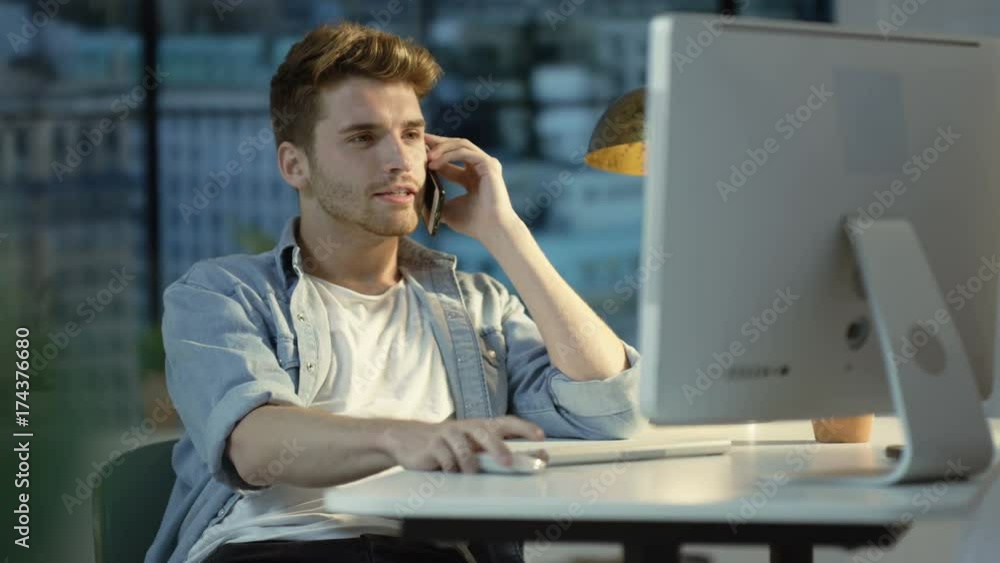 Young man using computer & talking on cell phone in city apartment Young man using computer & talking on cell phone in city apartment