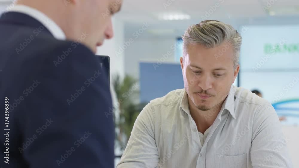 Modern city bank, man assisting customer & getting signature on document Modern city bank, man assisting customer & getting signature on document