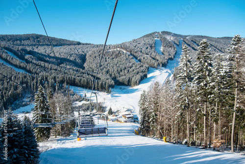 View from ski-lift at winter ski resort with an ideal landscape of snow-covered mountains, forests and ski slopes on a sunny day. Ski season and winter sports concept