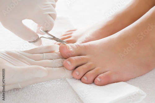Hands in gloves cares about a woman s foot nails. Pedicure  manicure beauty salon concept. Foot fingernails cutting with scissors.