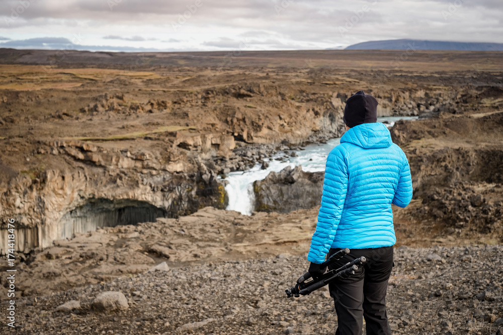 Fototapeta premium Female hiker looking at Aldeyjarfoss waterfall, Iceland. Female photographer holding a tripod.