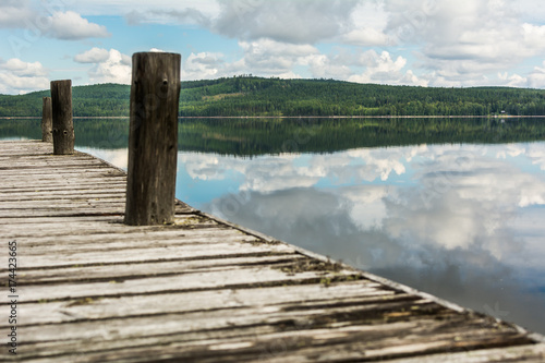 Old wooden pier on calm lake with reflection of mountains and cloudy sky. Dalarna region, Sweden
