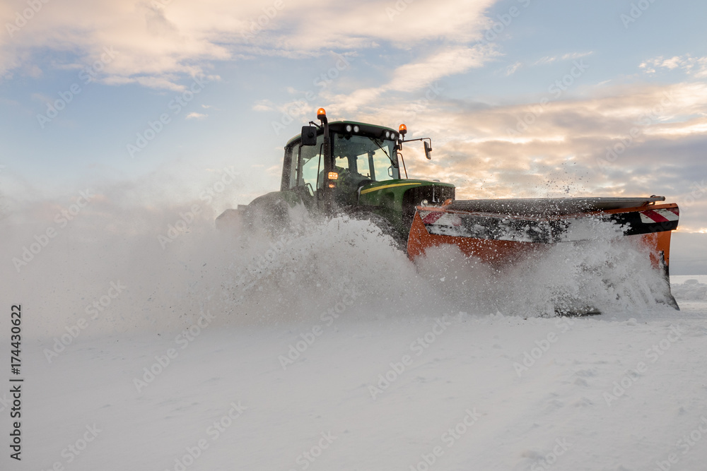 Fototapeta premium Traktor mit Schneepflug bei der Schneeräumung in Österreich. Landwirtschaftlich ausgerichtete Betriebe nutzen den Winter um Ihre Maschinen besser auslasten zu können.
