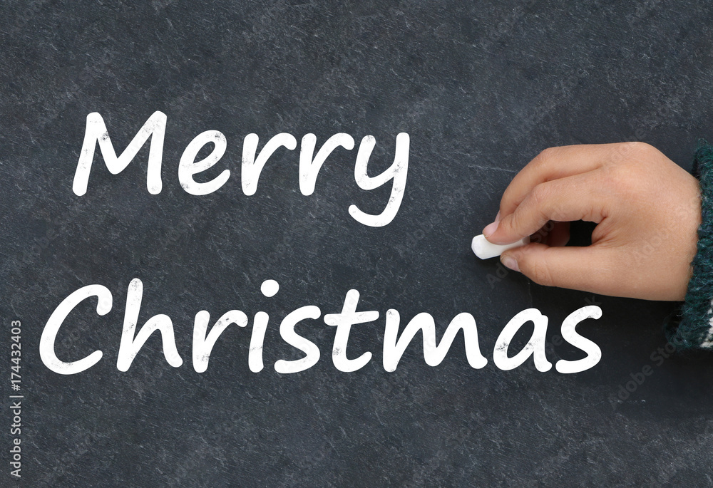 Fototapeta premium Little boy writing Merry Christmas on a blackboard