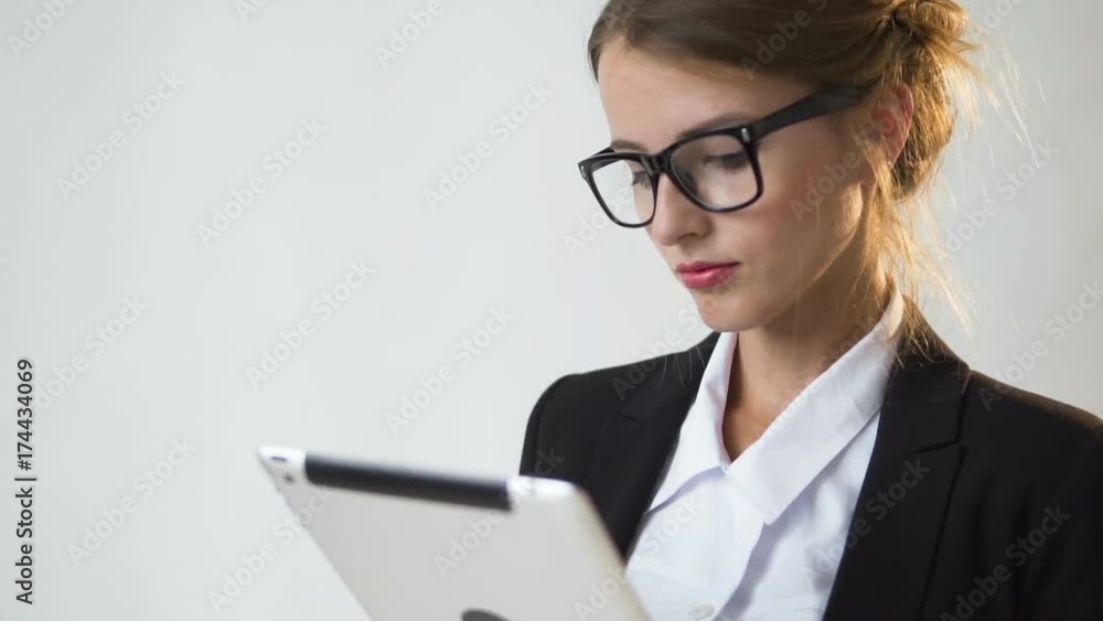 Occupied young dark hair caucasian businesswoman, in a white blouse and a black jacket, is using her tablet with pleasure in the white background, isolated, slow motion Occupied young dark hair caucasian businesswoman, in a white blouse and a black jacket, is using her tablet with pleasure in the white background, isolated, slow motion