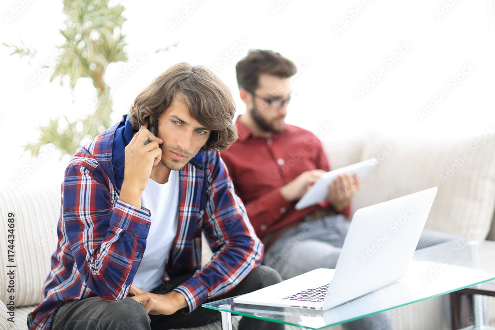 guy with a friend sitting on the couch, talking on the smartphone and searching for information on the Internet. guy with a friend sitting on the couch, talking on the smartphone and searching for information on the Internet.
