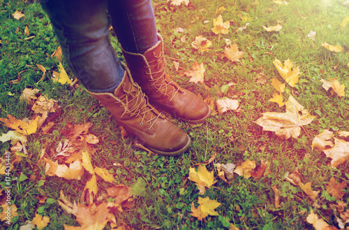 female feet in boots and autumn leaves on grass