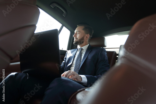 businessman working with laptop and looking out the window of a car