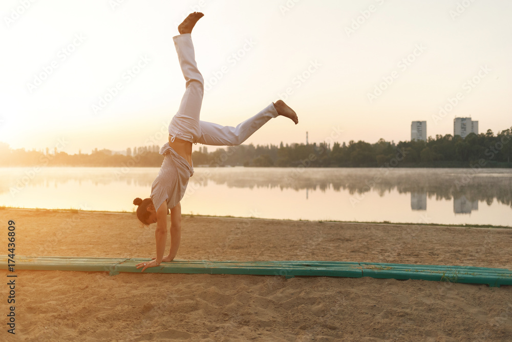Fototapeta premium Athletic capoeira performer workout training on the beach sunris