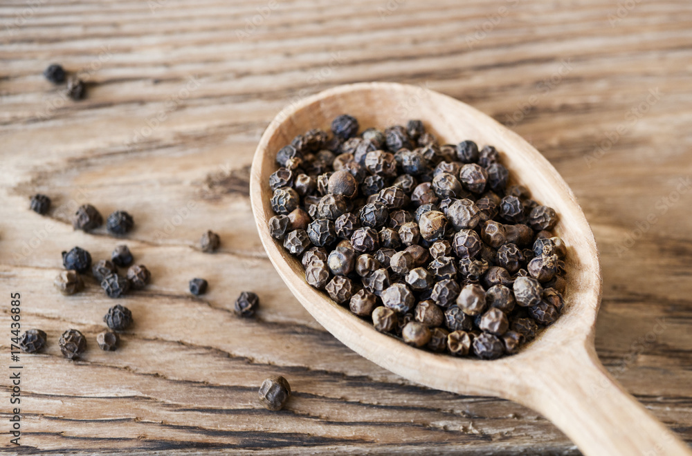 Black peppercorns in wooden spoon on rustic table Black peppercorns in wooden spoon on rustic table