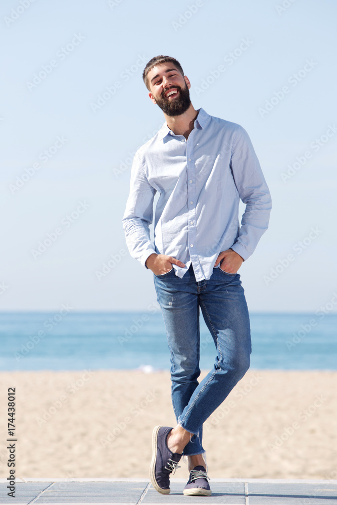 Full length confident man laughing and standing on beach Full length confident man laughing and standing on beach