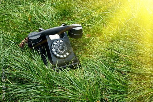 Black old retro telephone in the grass with sunshine beams