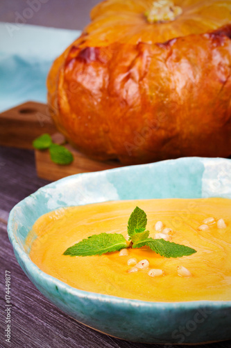 Creamy pumpkin (or butternut squash) soup in a bowl, whole roasted pumpkin on wooden background, vertical