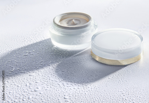 The jar of cosmetic moisturizing cream on the white background with water drops around the jar