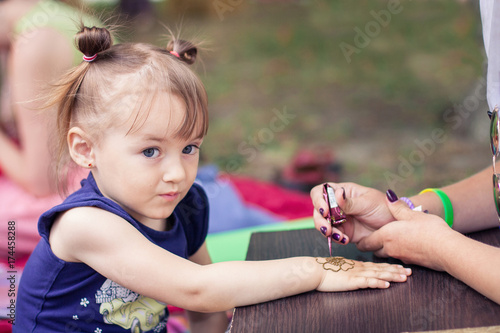 Woman mehendi artist painting henna on the child's hand