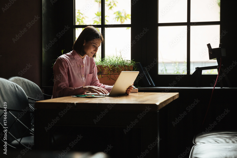 Smiling woman sitting by table in cafe and using laptop Smiling woman sitting by table in cafe and using laptop
