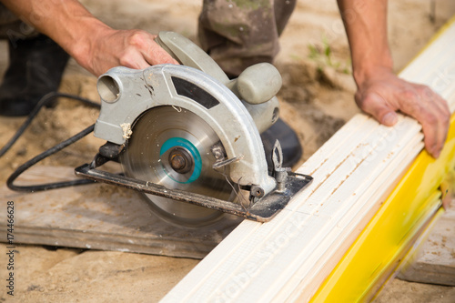worker saws a wooden plank at a construction site