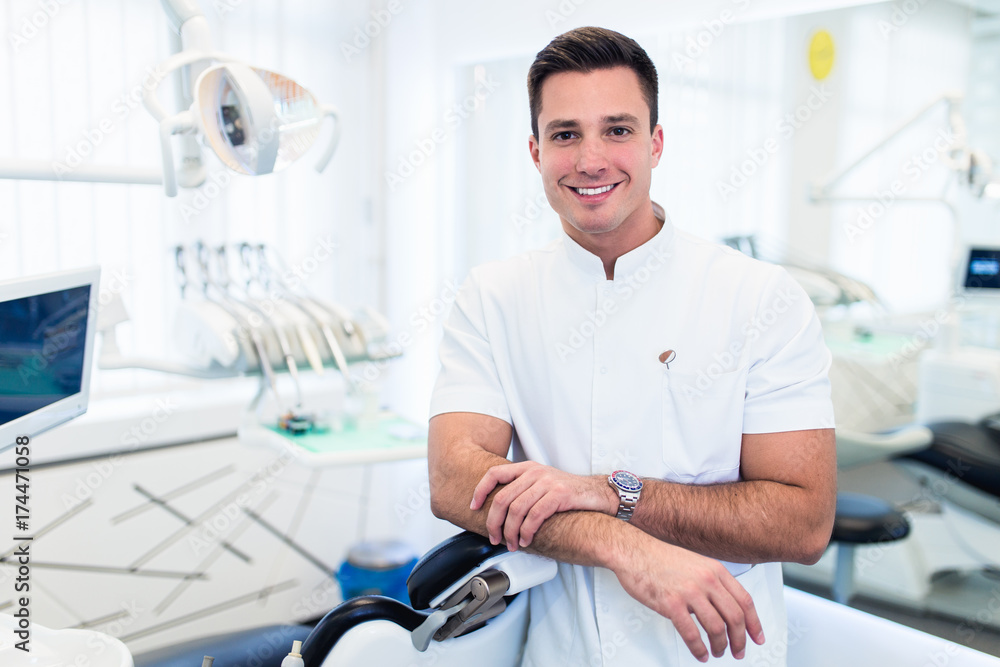 Attractive male dentist in doctors white lab coat posing in modern