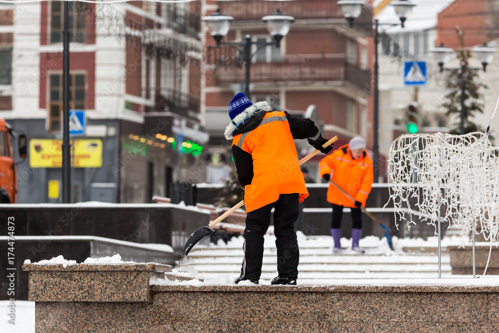 People-janitors in orange jackets cleaned the city from snow with shovels. Winter city after a snowfall.