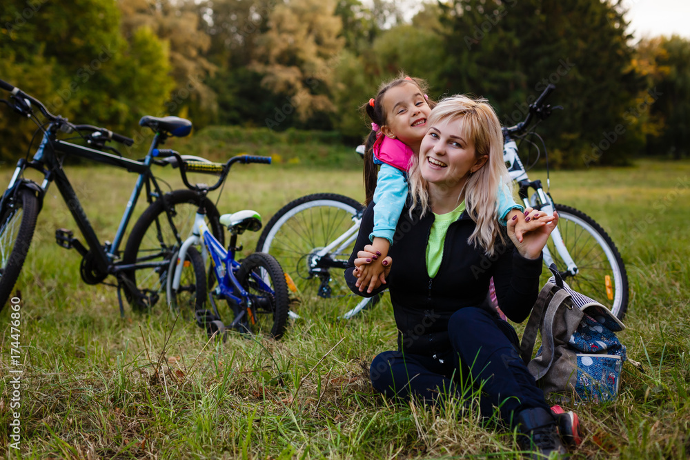 Young mother with her daughter resting in a park near their bike