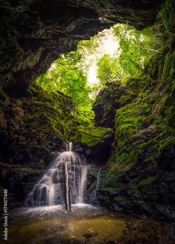 Waterfall and rocks covered with moss in a forest cave