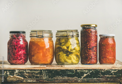 Autumn seasonal pickled or fermented colorful vegetables in jars placed in row over vintage kitchen drawer, white wall background, copy space. Fall home food preserving or canning