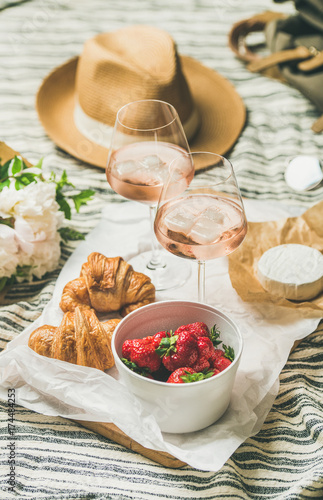 French style romantic summer picnic setting. Flat-lay of glasses of rose wine with ice, strawberries in bowl, croissants, brie cheese, straw hat, peony flowers, square crop. Outdoor gathering concept