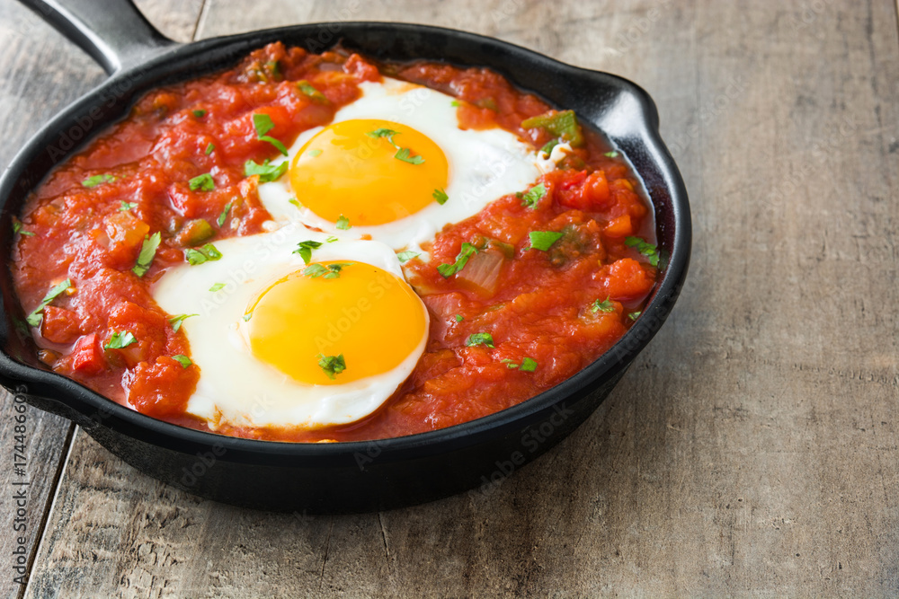 Mexican breakfast: Huevos rancheros in iron frying pan on wooden table